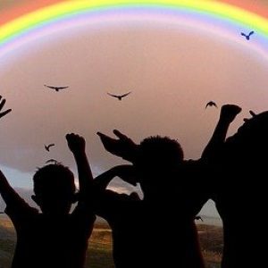 A silhouette of people raising their hands and looking at the rainbow